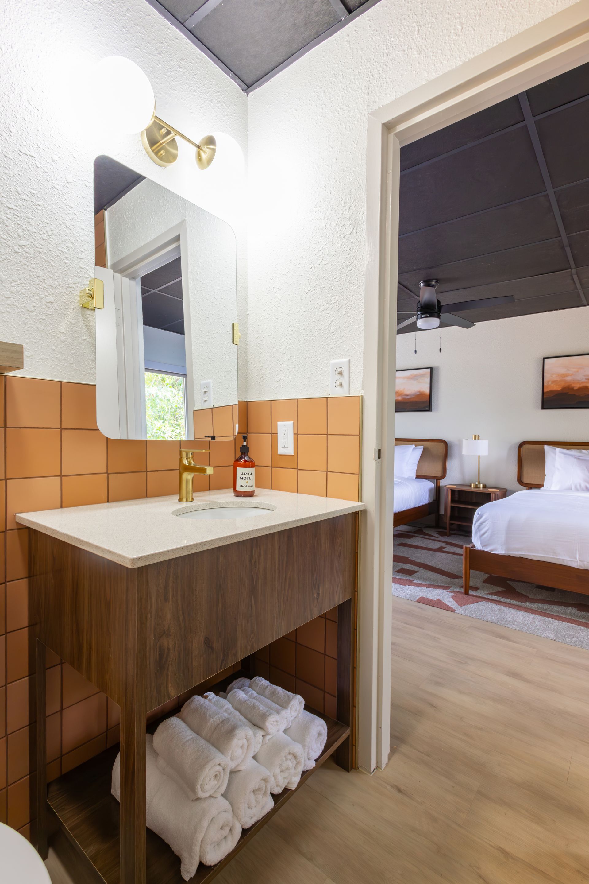 A bathroom with terracotta colored tile and a wooden modern vanity with a view of the bedroom.
