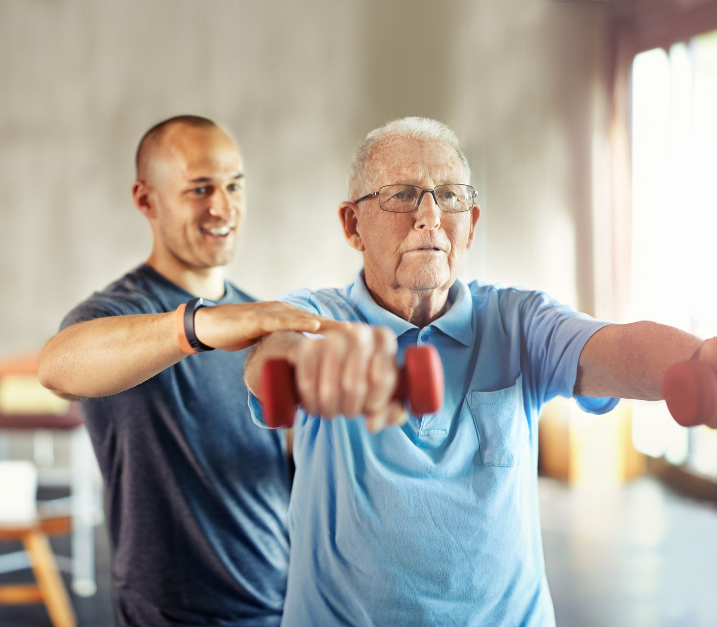 Physiotherapist supporting an older man with strength exercises at home