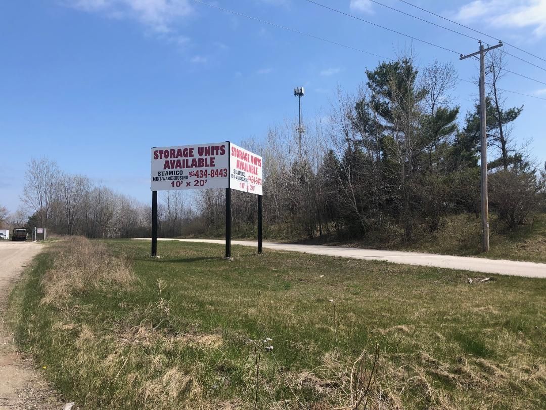 A sign for storage units is sitting on the side of a dirt road.