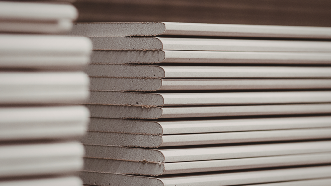 A stack of white gypsum drywall panels viewed from the side, showing their layered, rectangular structure.