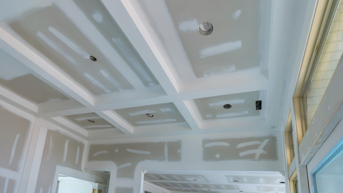 A partially finished coffered ceiling with drywall installed and mudded, ready for final sanding and painting.