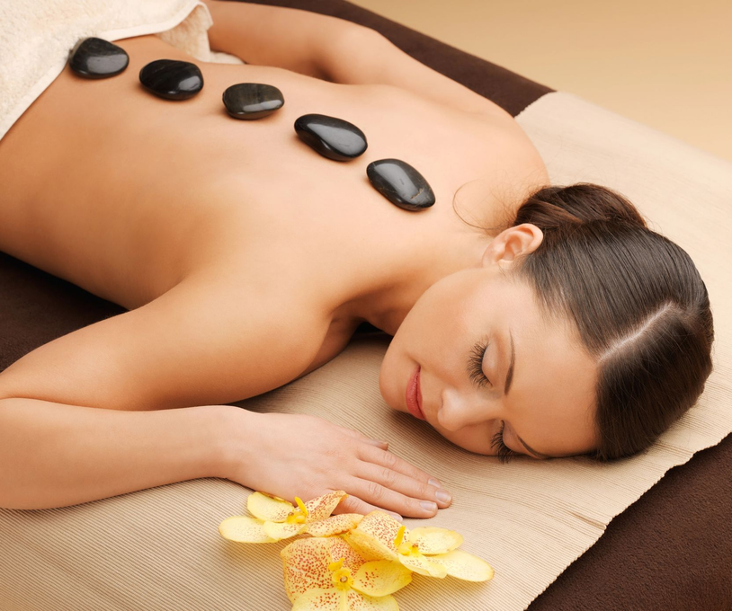 Una mujer tumbada en una camilla de masaje con piedras calientes en la espalda y flores cerca.