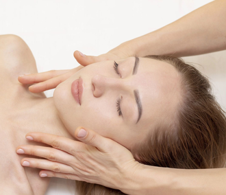 Persona que recibe un masaje facial con los ojos cerrados, con las manos sosteniendo suavemente el rostro.