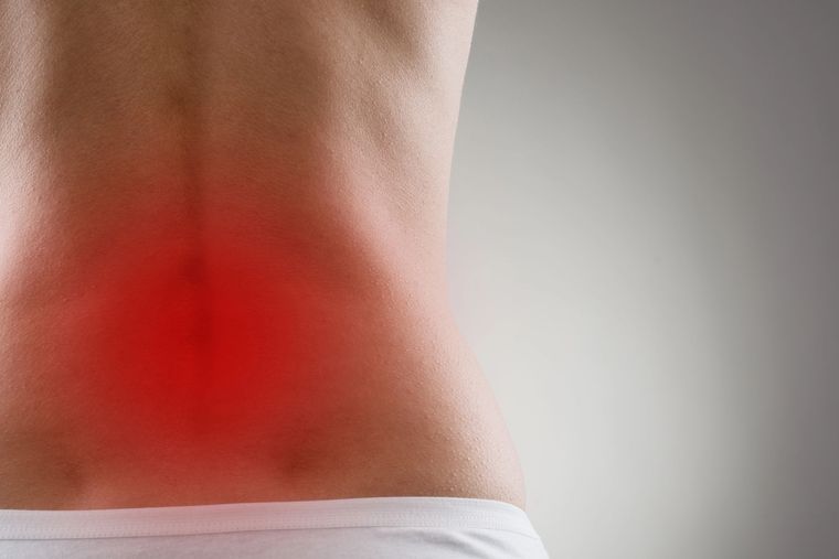 Persona sujetándose la parte baja de la espalda, con la zona dolorida resaltada en rojo.