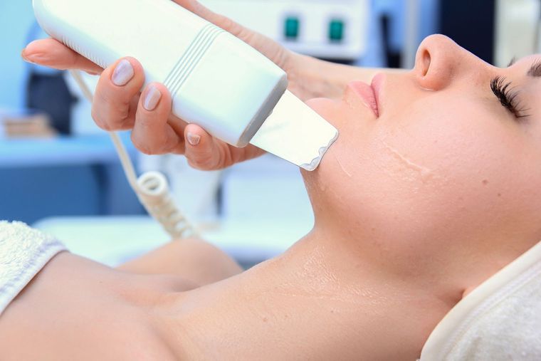 Tratamiento facial con un dispositivo manual aplicado en la mejilla de una mujer en un entorno de spa.