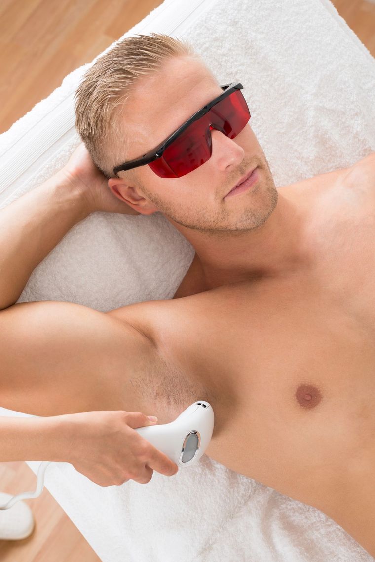 Un hombre recibe un tratamiento de pecho con una varita de terapia de luz roja mientras usa gafas protectoras rojas.