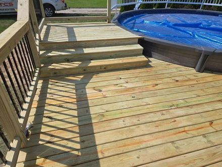 Wooden deck with steps leading to an above-ground pool, visible blue pool cover, and sunlight.