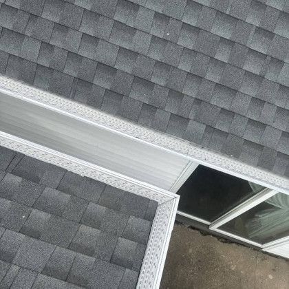 Gray shingle roof with a silver gutter, next to a white-framed window.