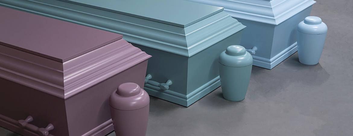 Three colorful coffins with matching urns arranged on a reflective surface.