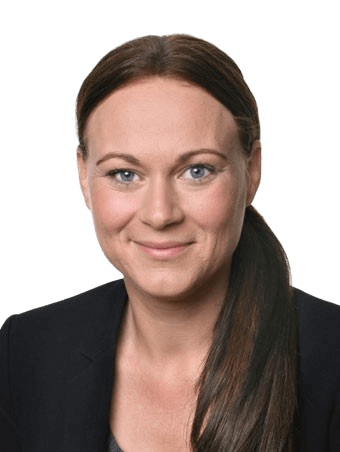 Woman with brown hair in a low ponytail, smiling. Wearing a dark blazer, neutral background.