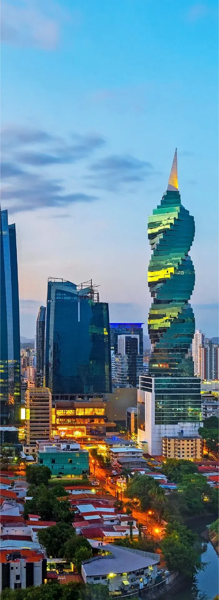 Una vista aérea del horizonte de una ciudad por la noche con un edificio muy alto en primer plano.