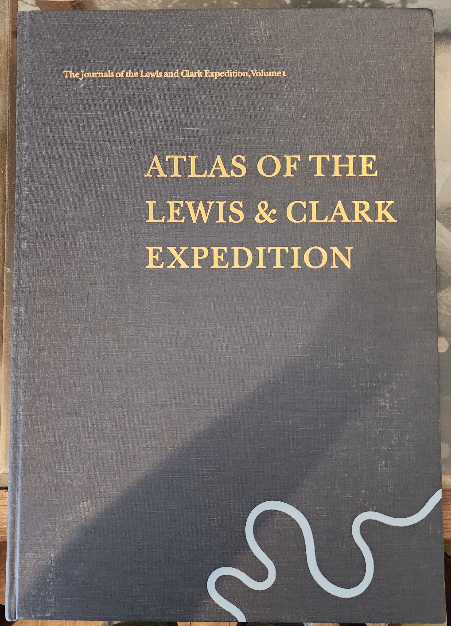 Gray book cover titled “Atlas of the Lewis & Clark Expedition” with a white squiggle at the bottom right