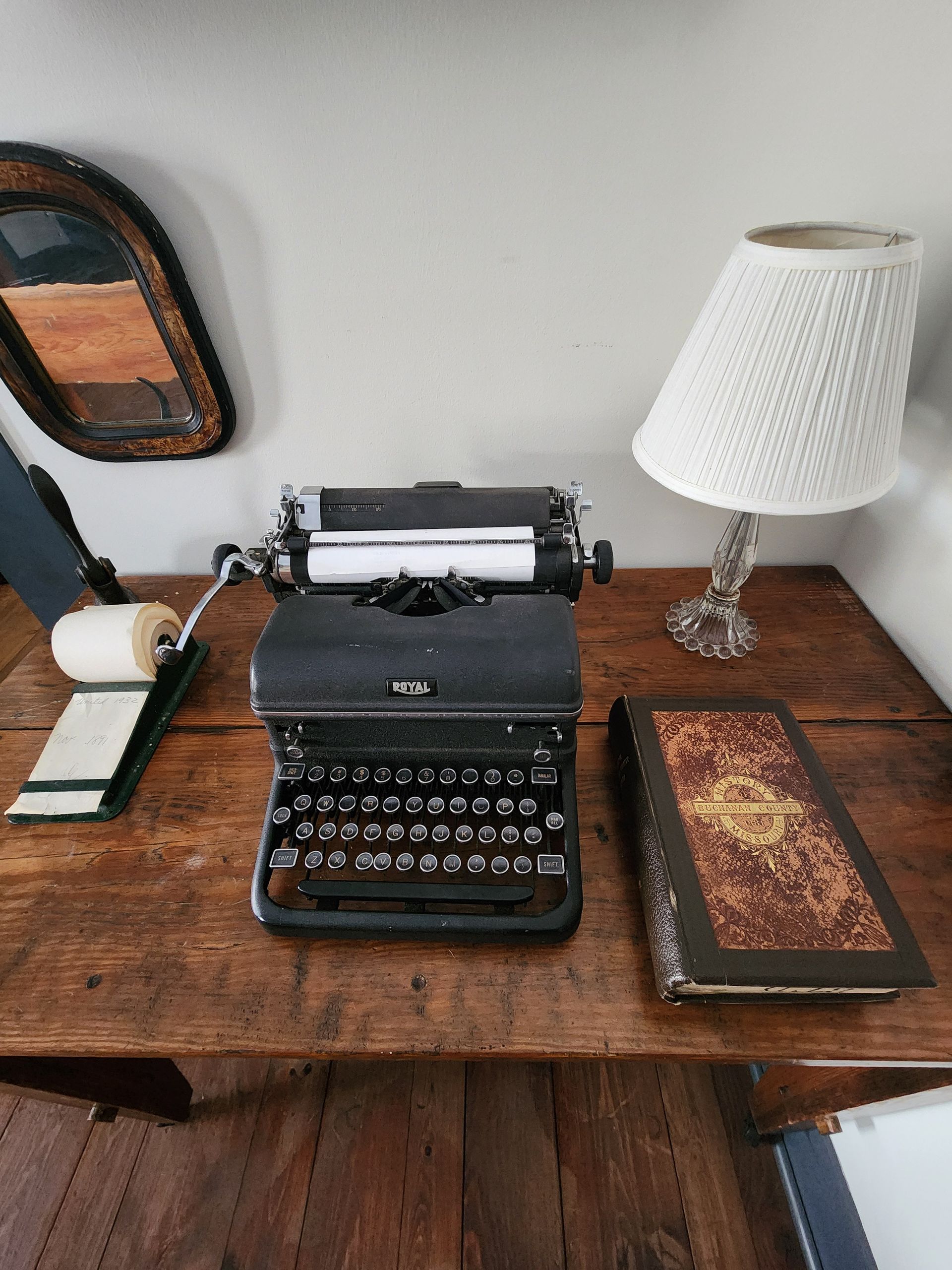 Vintage black typewriter on a wooden desk beside a patterned book and lamp.