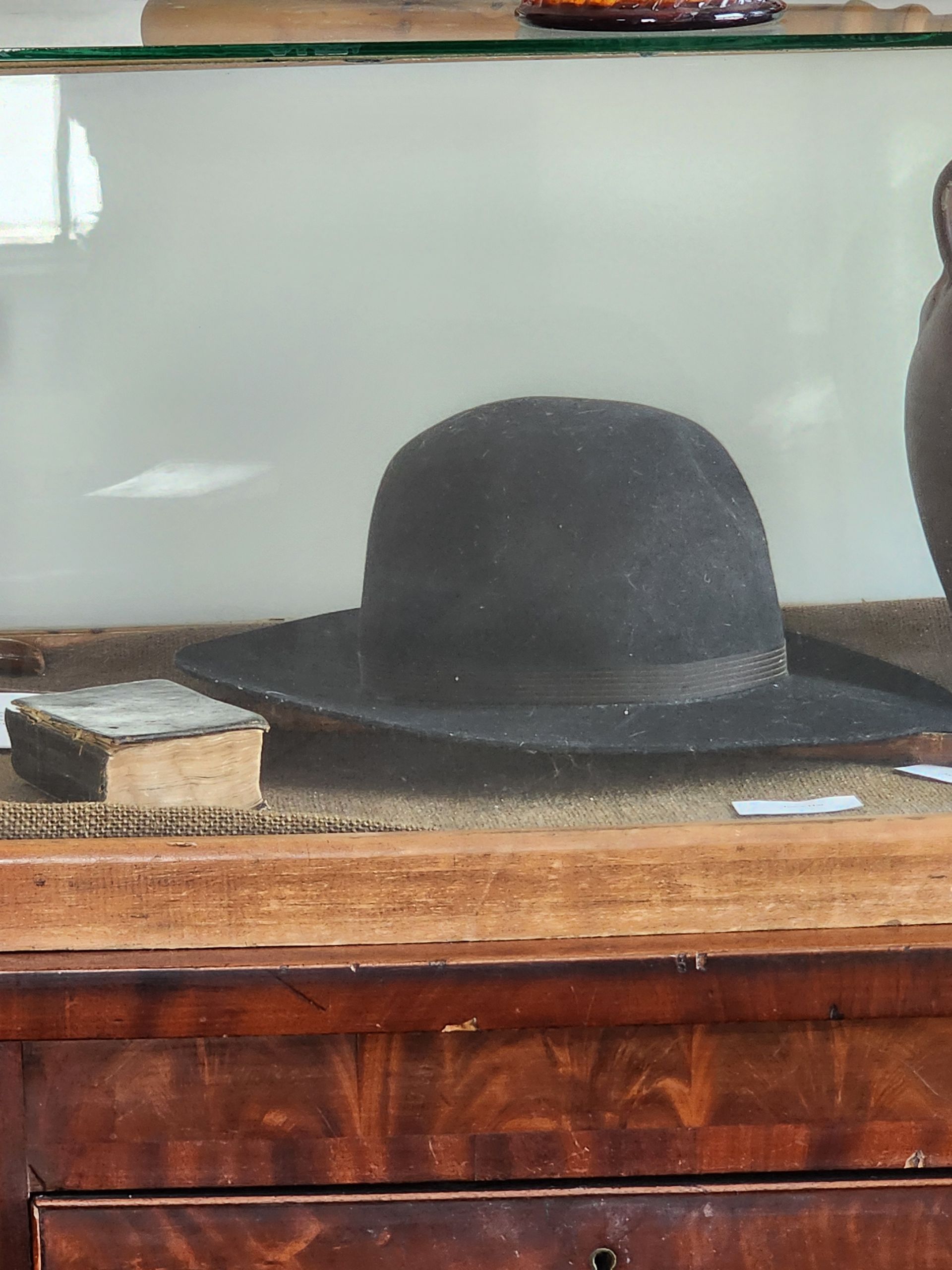 Black hat on a wooden shelf in front of a mirror, with a small box beside it.