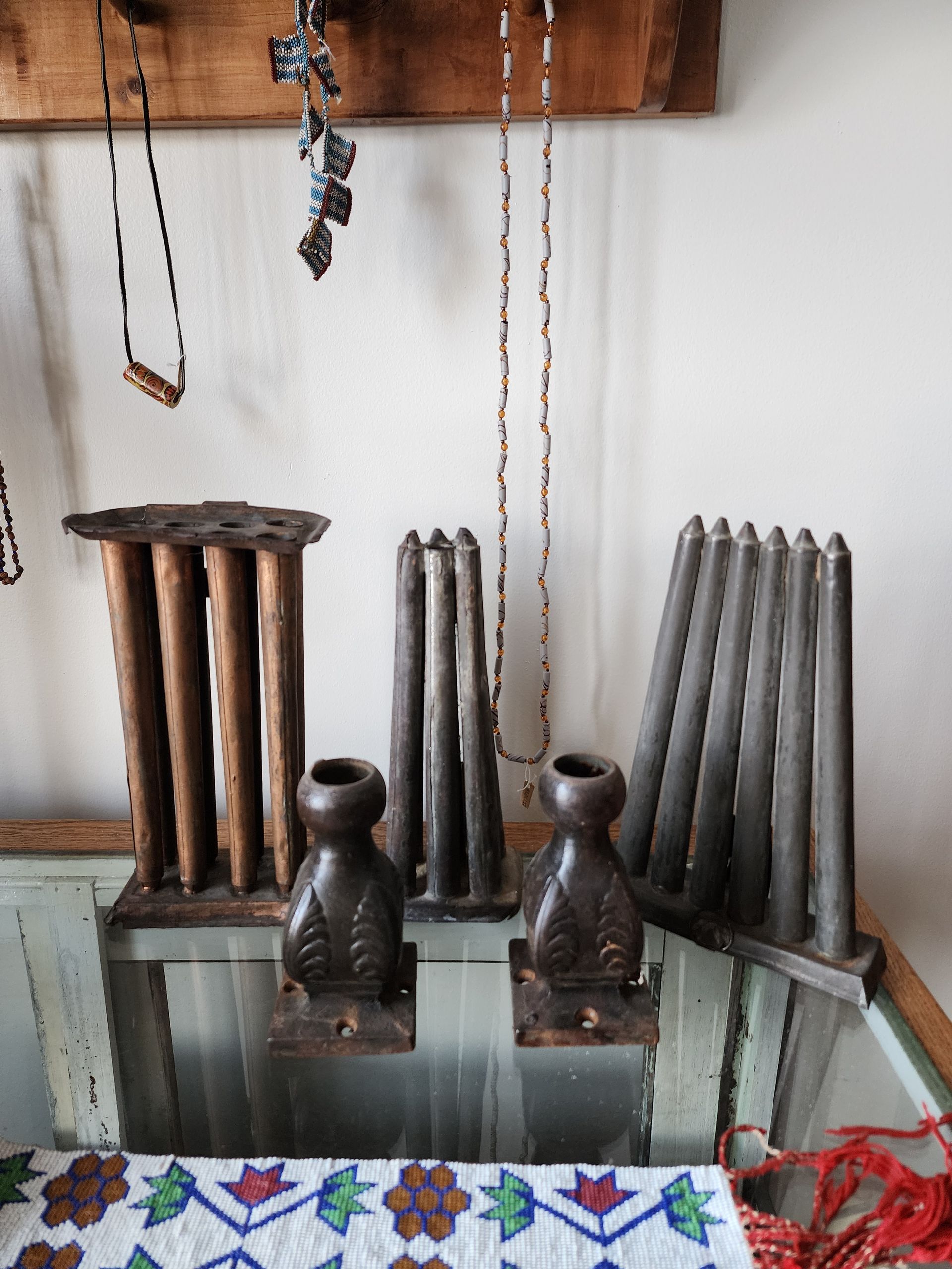 Old metal machine parts displayed on a shelf against a white wall, with a colorful cloth below.