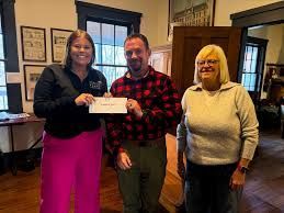 Three people indoors holding a check, smiling in a wood-paneled room.