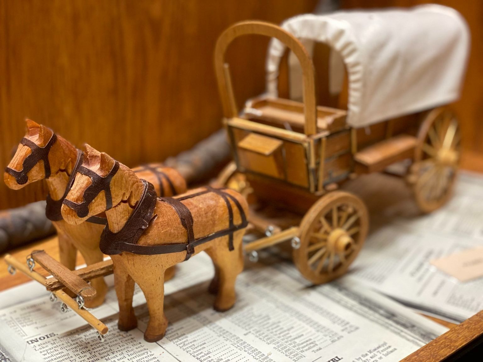 Wooden horse-drawn cart model on sheet music, with a wagon and harnessed horses.