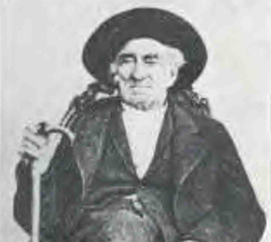 Black-and-white portrait of an elderly man in a wide-brimmed hat, seated and holding a walking stick