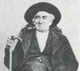 Black-and-white portrait of an elderly man in a wide-brimmed hat, seated and holding a walking stick