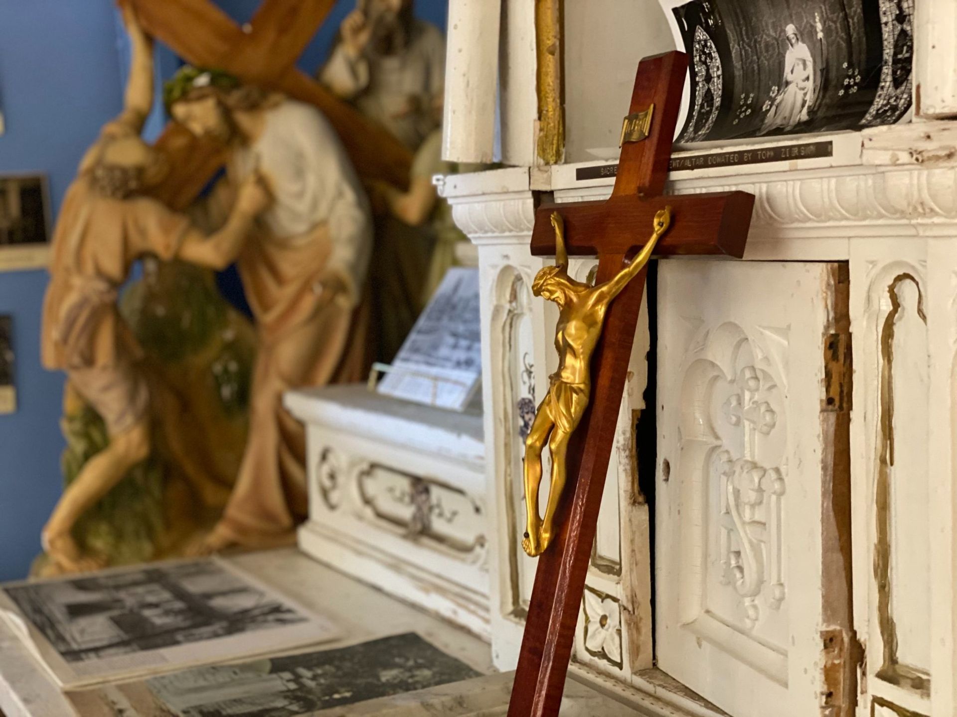 Crucifix with gold Jesus figure on a white altar beside a religious painting and statue