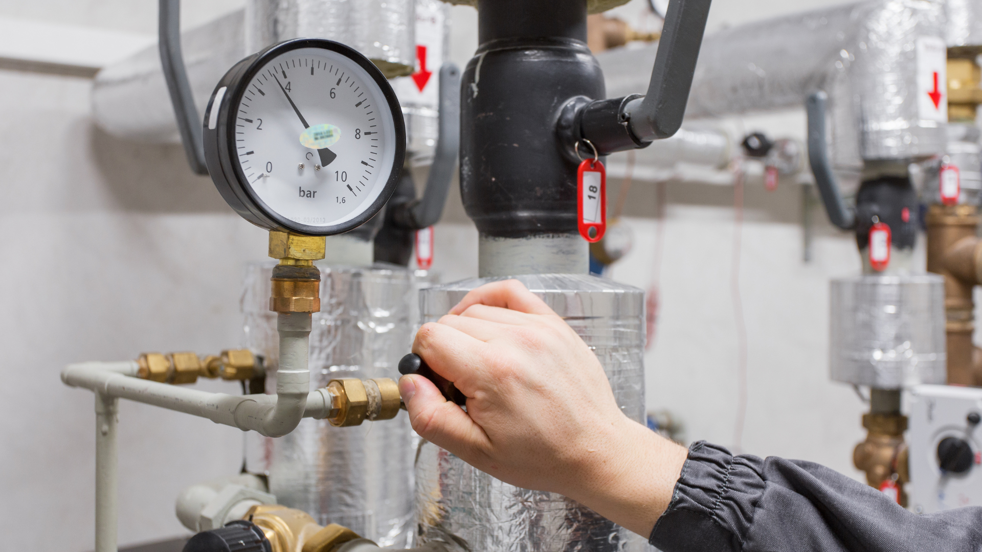 A person is working on a pressure gauge in a boiler room.