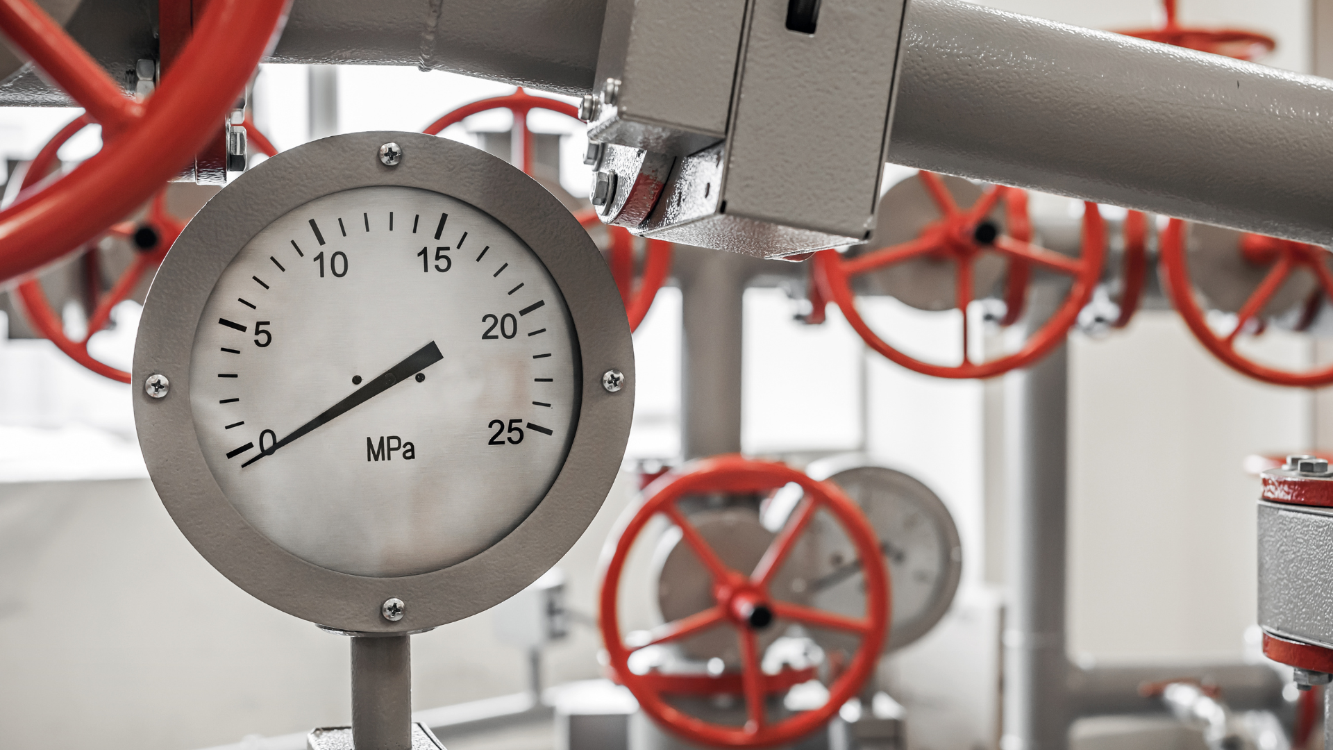 A close up of a pressure gauge in a factory with red valves.