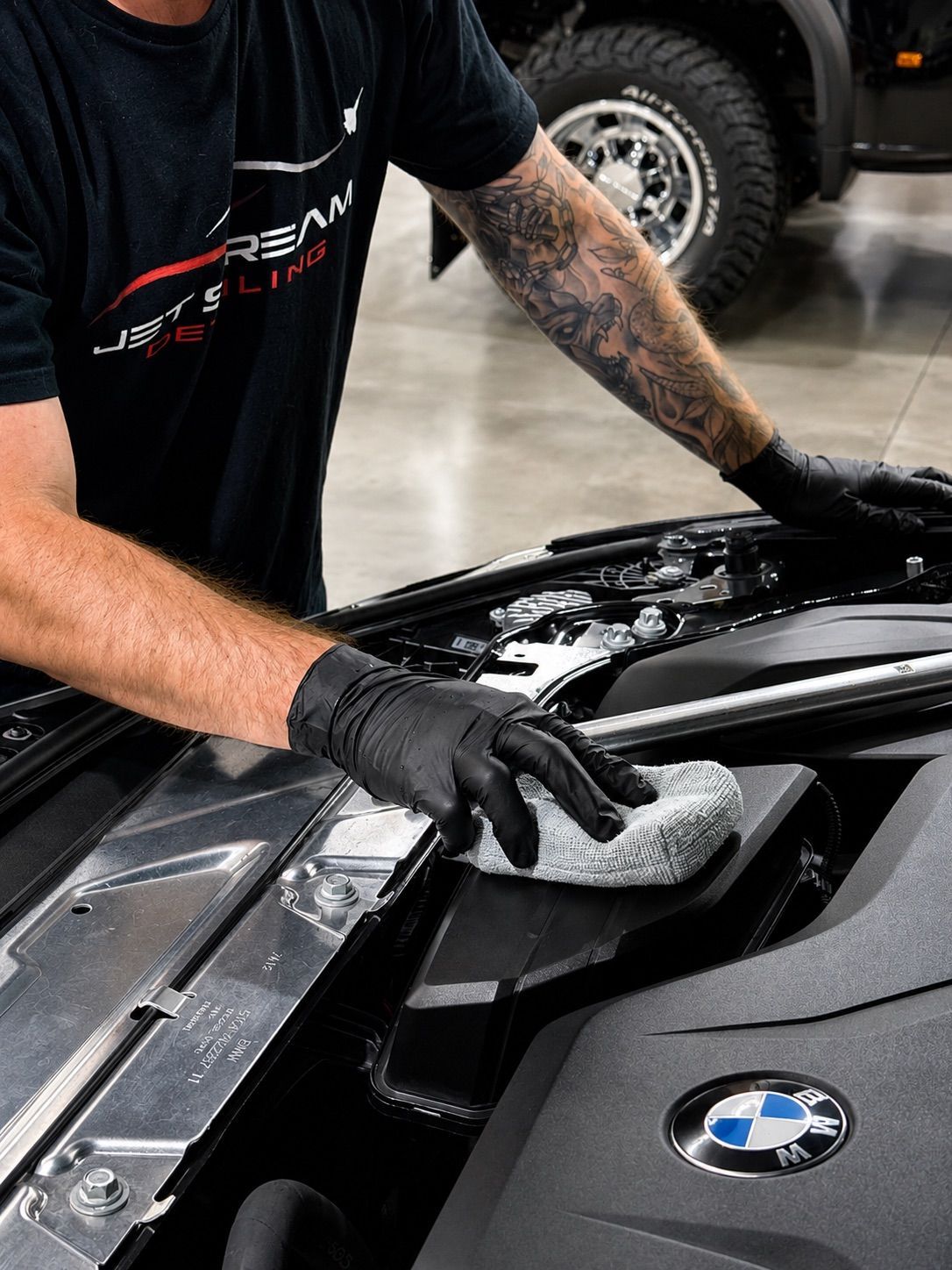 Detailing technician wiping a black BMW hood with a microfiber cloth in a garage