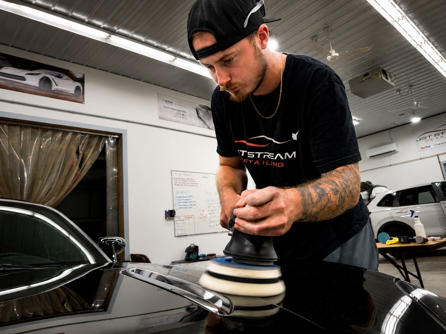 Technician polishing a black car with a buffer in an auto shop
