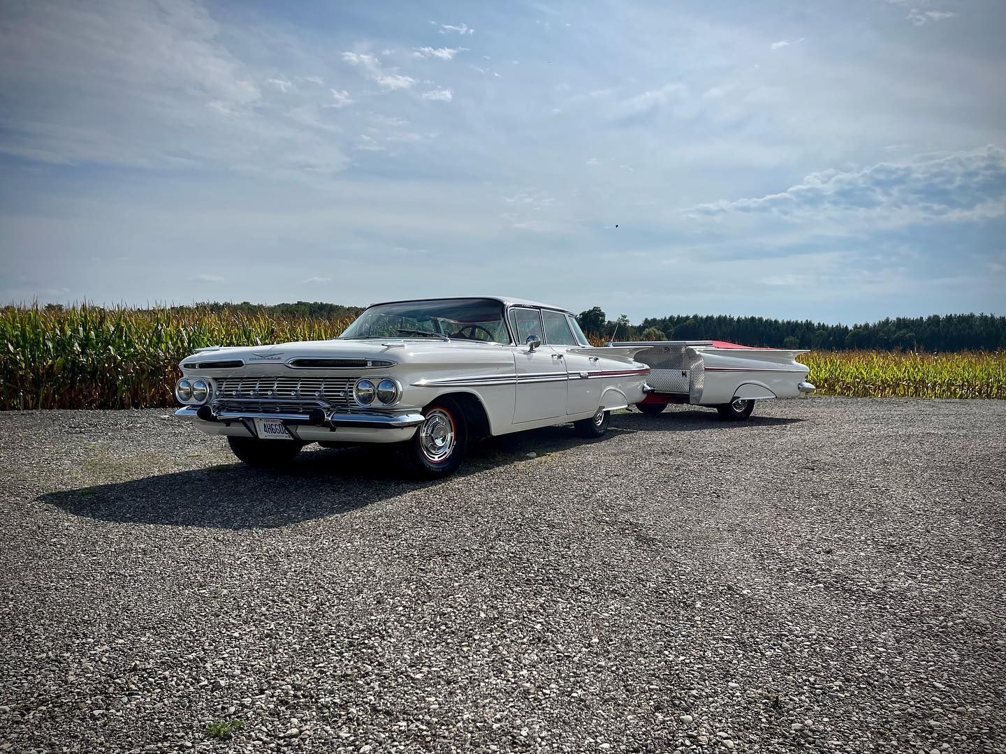 A white car with a trailer attached to it is parked in a gravel lot.