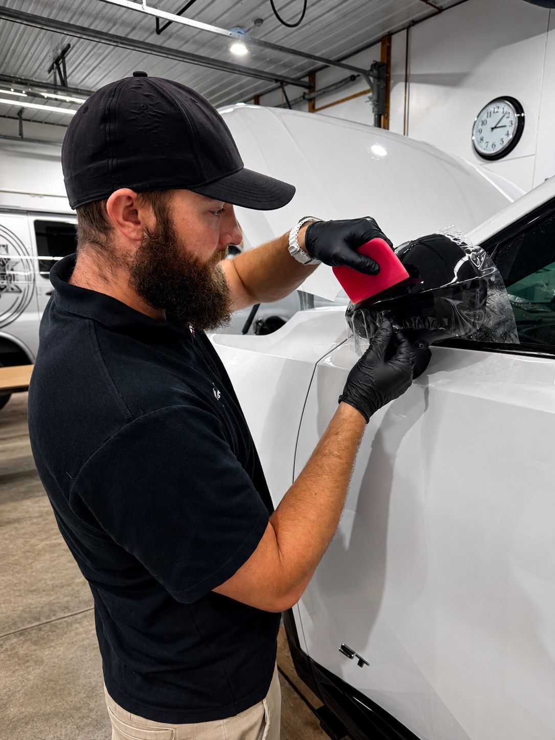 Person polishing a white car with a red buffer in an auto shop
