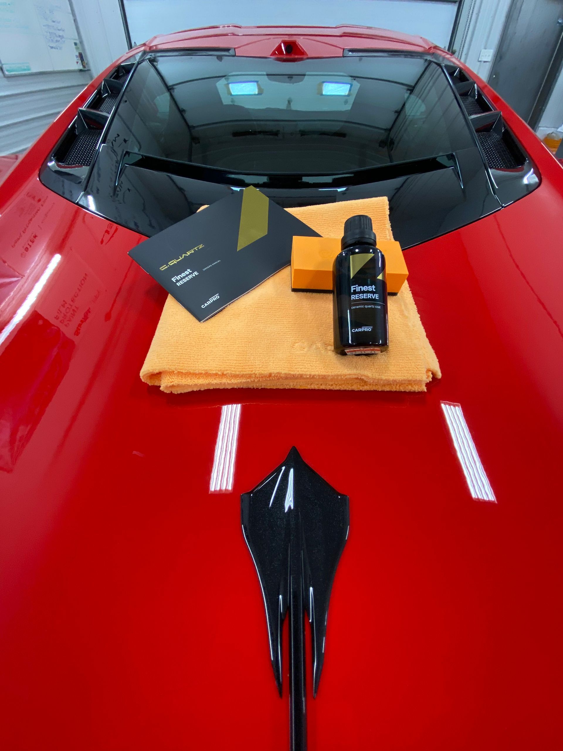 A red car with a towel and a bottle of polish on the hood.