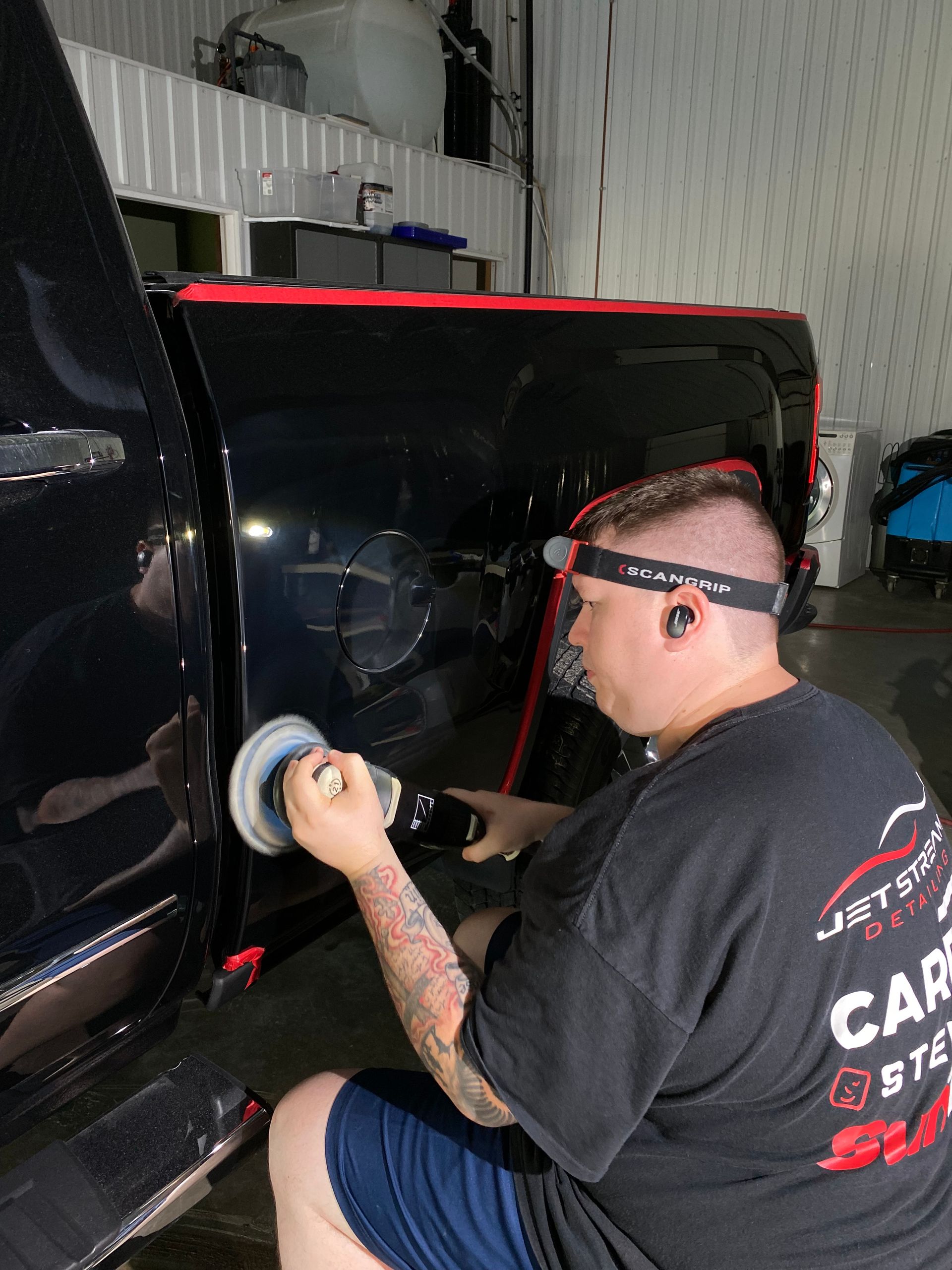 A man is polishing the side of a black truck.