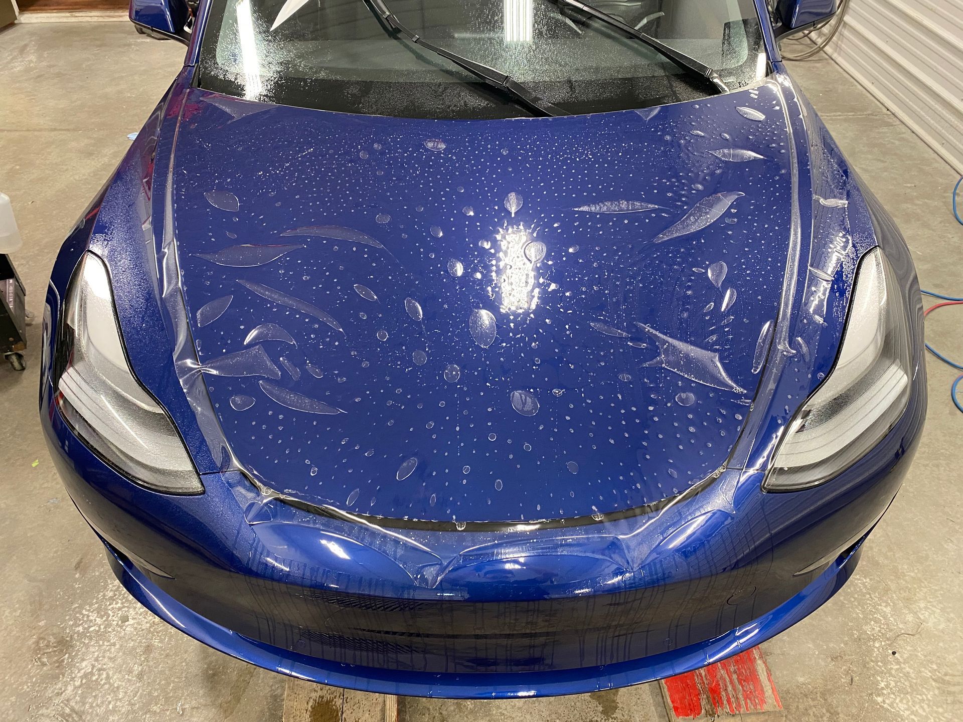 A blue tesla model 3 is wrapped in plastic.