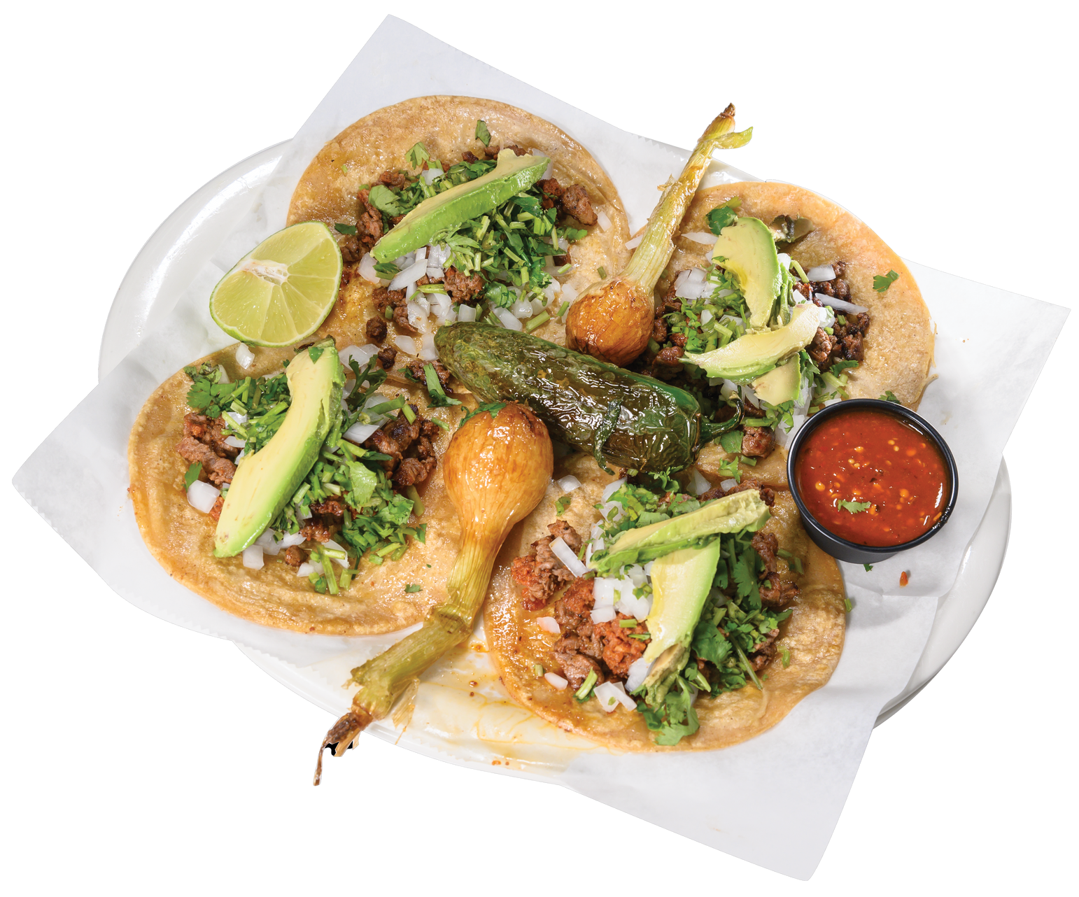 Tacos on a plate with avocado, cilantro, onion, and salsa; garnished with lime and peppers.