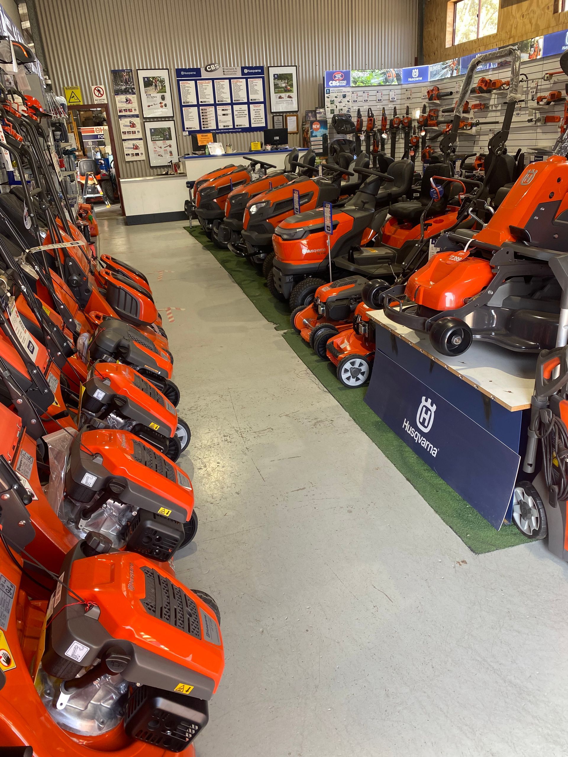 Rows of orange lawn mowers displayed in a store, with other gardening equipment in the background. — CBS Chainsaw & Brushcutter Specialists - HUSQVARNA in Wauchope, NSW