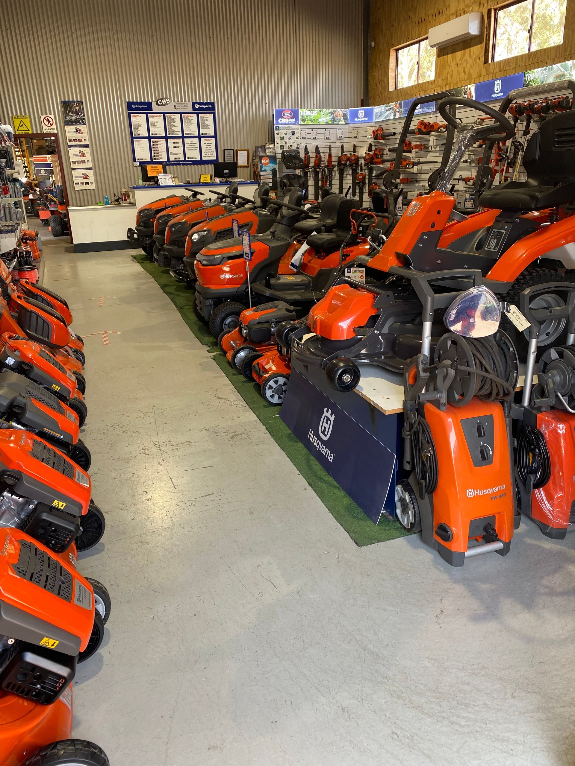 Rows of orange lawnmowers displayed inside a retail store, with other equipment and signage visible. — CBS Chainsaw & Brushcutter Specialists - HUSQVARNA in Wauchope, NSW