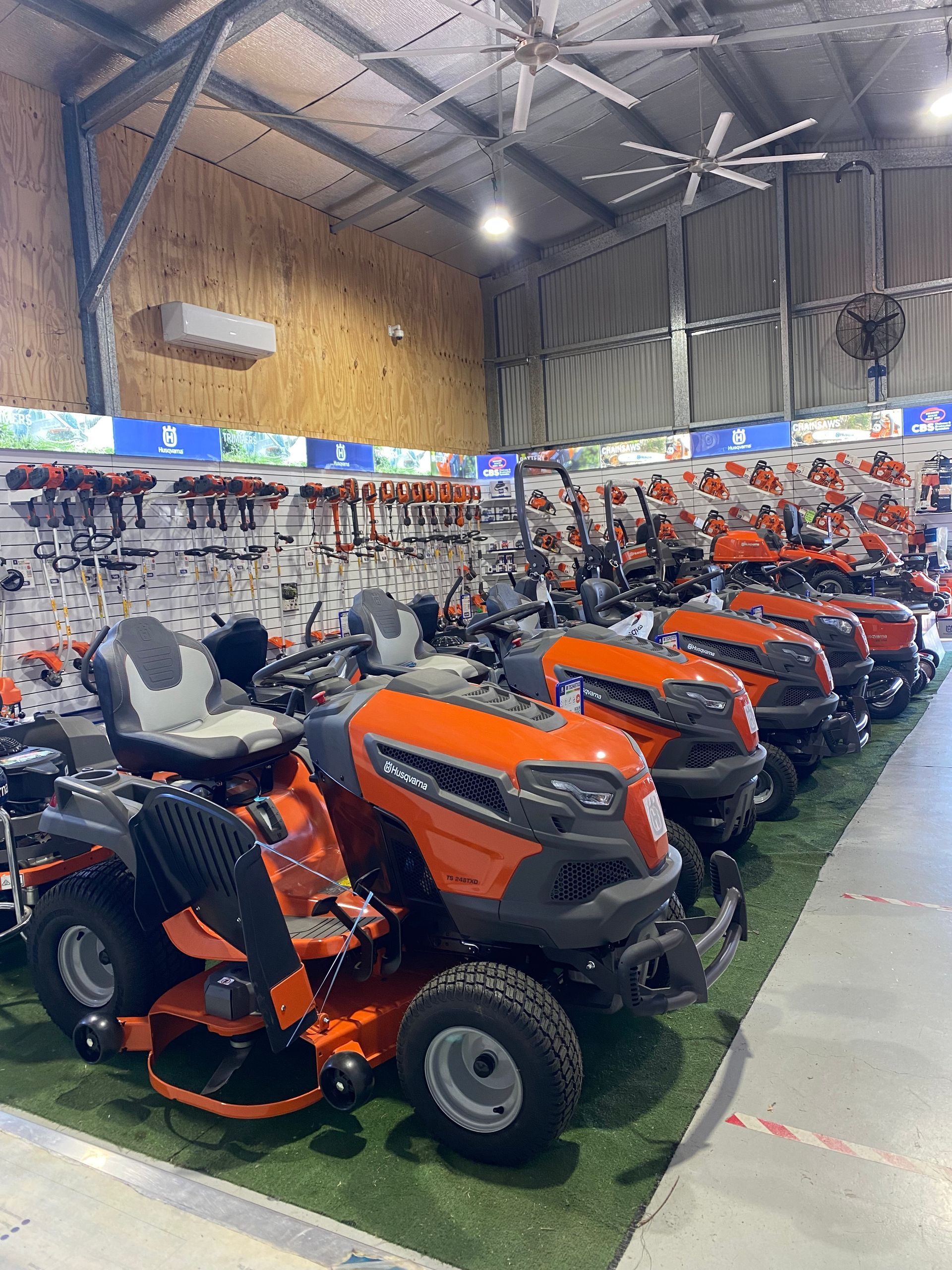 Row of orange and black lawn tractors displayed in a hardware store, with other tools visible on the walls. — CBS Chainsaw & Brushcutter Specialists - HUSQVARNA in Wauchope, NSW
