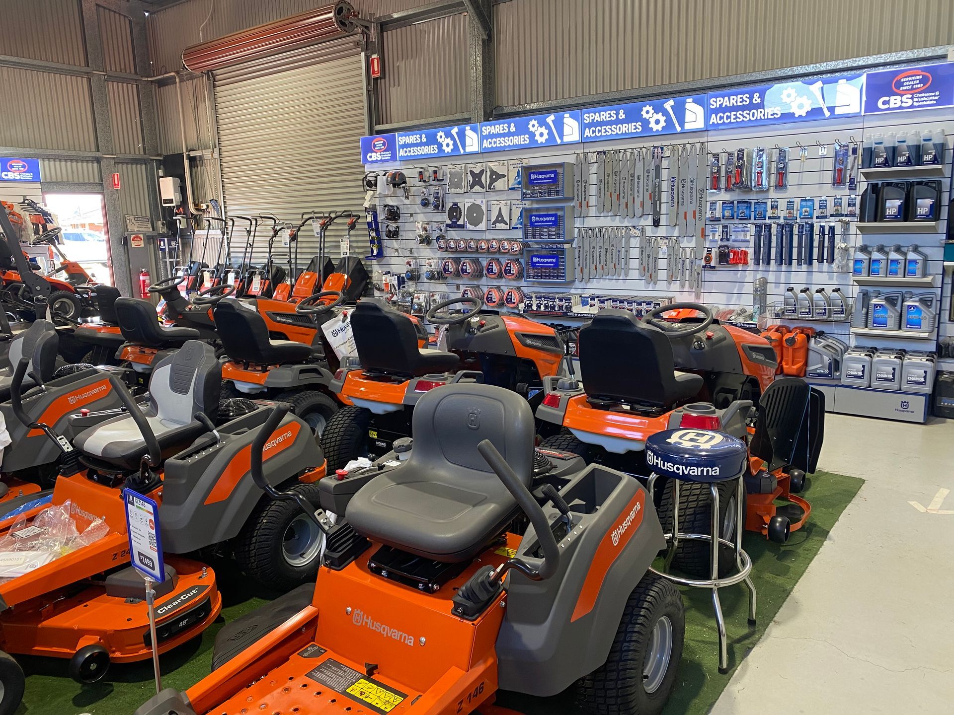 Inside a store, several orange and black riding lawnmowers are on display. Shelves with tools and accessories are in the background. — CBS Chainsaw & Brushcutter Specialists - HUSQVARNA in Wauchope, NSW