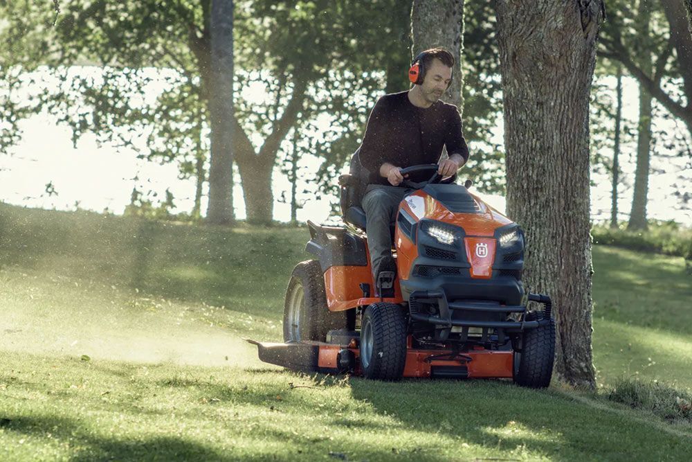 A Man Is Riding a Lawn Mower in A Park — CBS Chainsaw & Brushcutter Specialists - HUSQVARNA in Port Macquarie, NSW