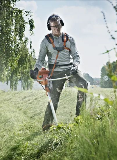 A Man Is Using a Lawn Mower to Cut Grass in A Field — CBS Chainsaw & Brushcutter Specialists - HUSQVARNA in Wauchope, NSW