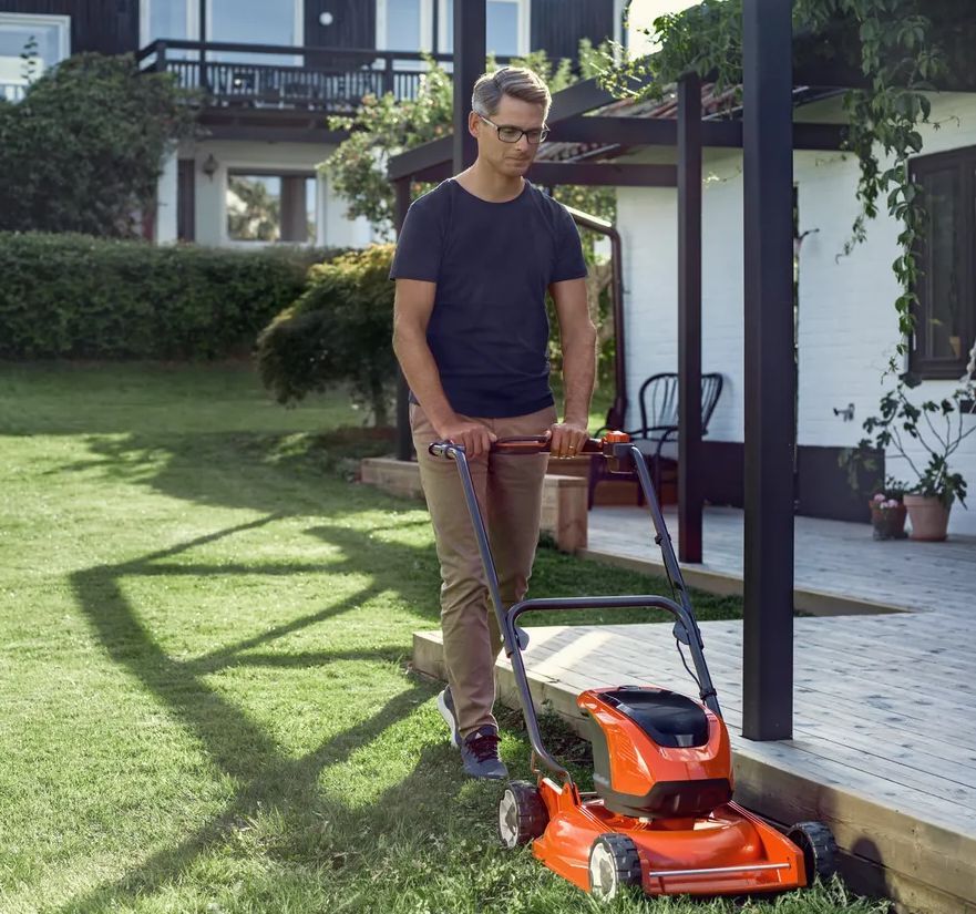 A Man Is Pushig a Lawn Mower Next to A House — CBS Chainsaw & Brushcutter Specialists - HUSQVARNA in Wauchope, NSW