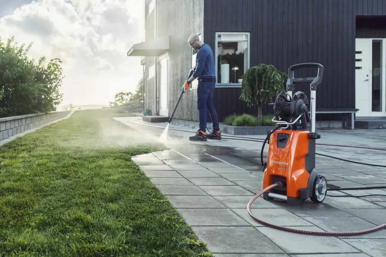A Man Is Using a High Pressure Washer to Clean a Sidewalk in Front of A House — CBS Chainsaw & Brushcutter Specialists - HUSQVARNA in Wauchope, NSW