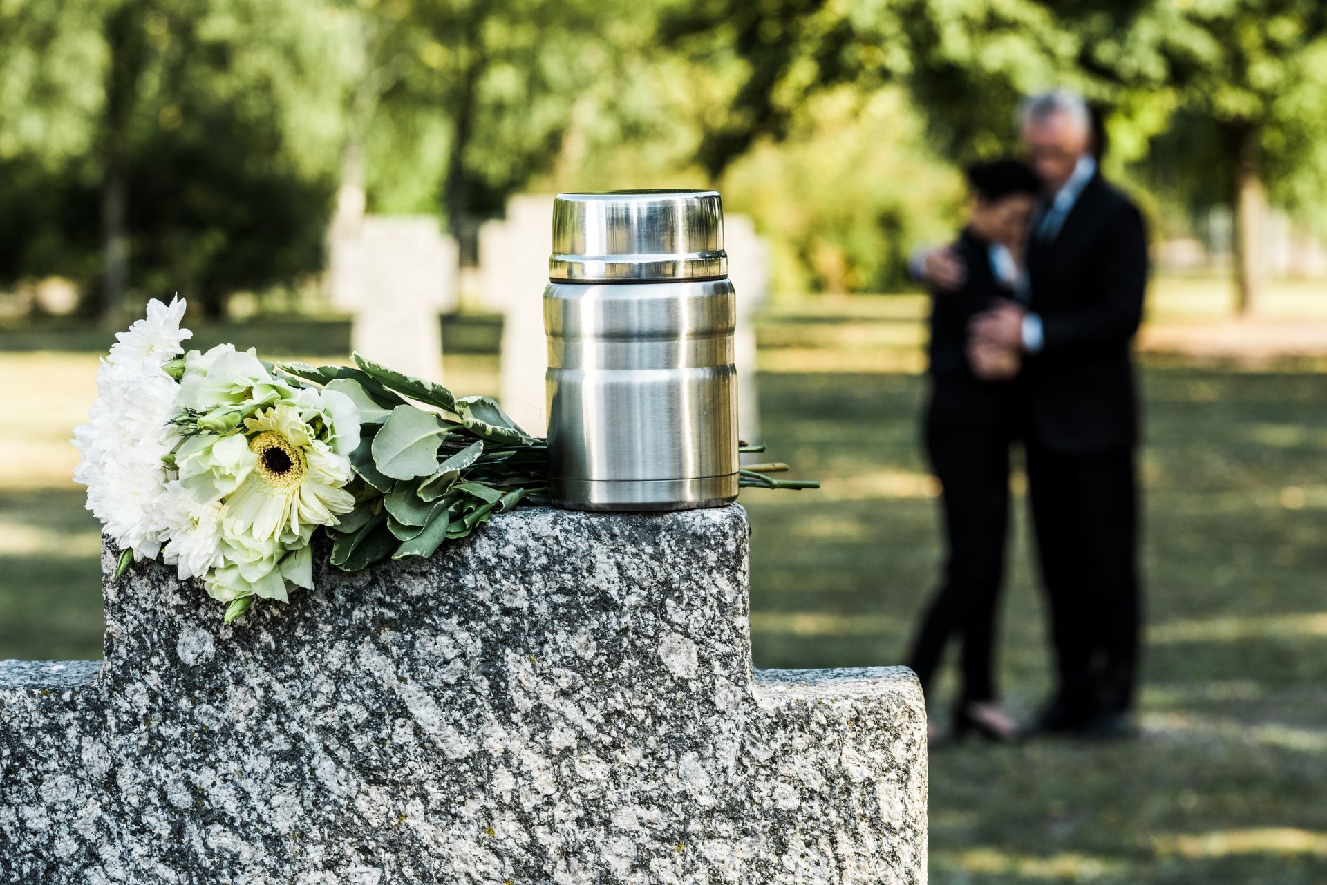 selective focus of white flowers and cemetery urn on tombstone  