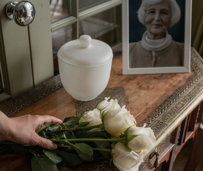 Urn, bouquet of white roses, a picture of an older woman, resting on an antique piece.