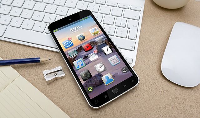 A smart phone is sitting on a desk next to a keyboard and mouse.