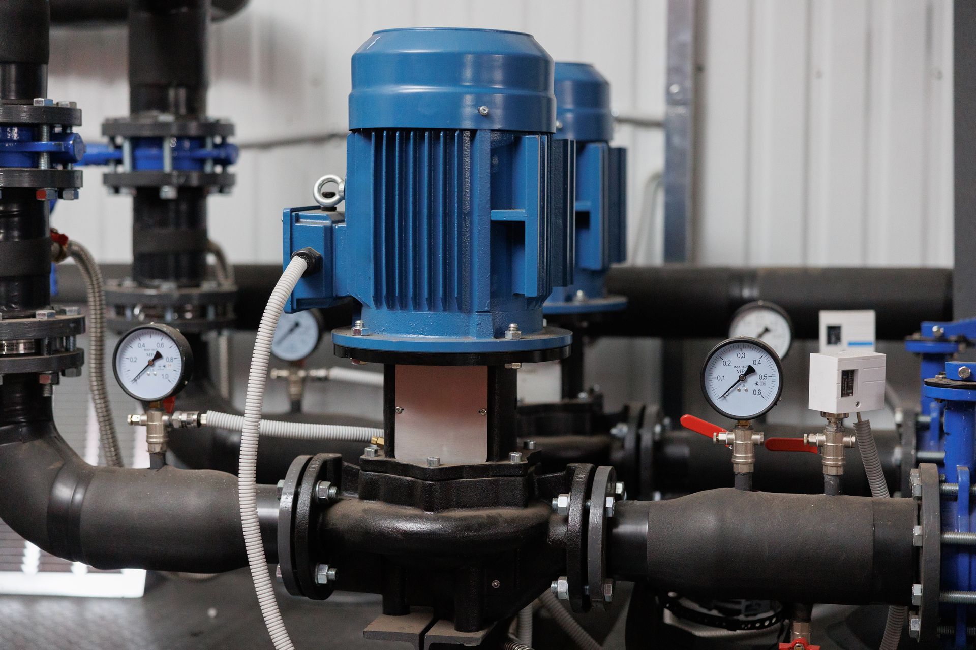 Blue industrial motor mounted on black pipes with pressure gauges in a mechanical room