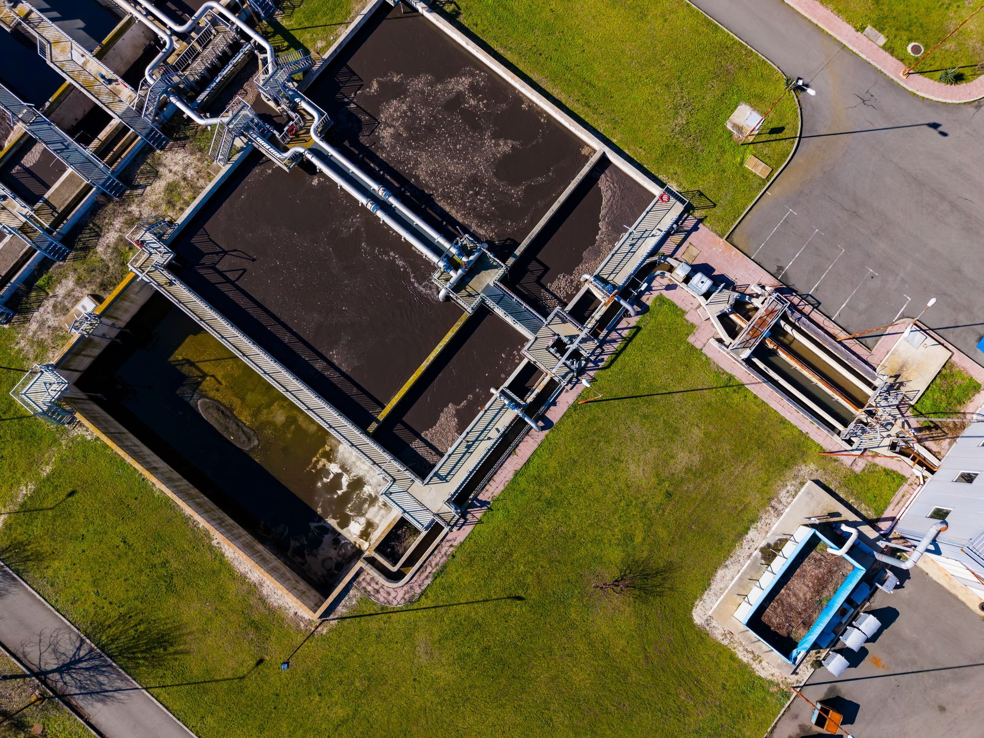 Aerial view of a water treatment plant with large tanks, pipes, and surrounding grass.