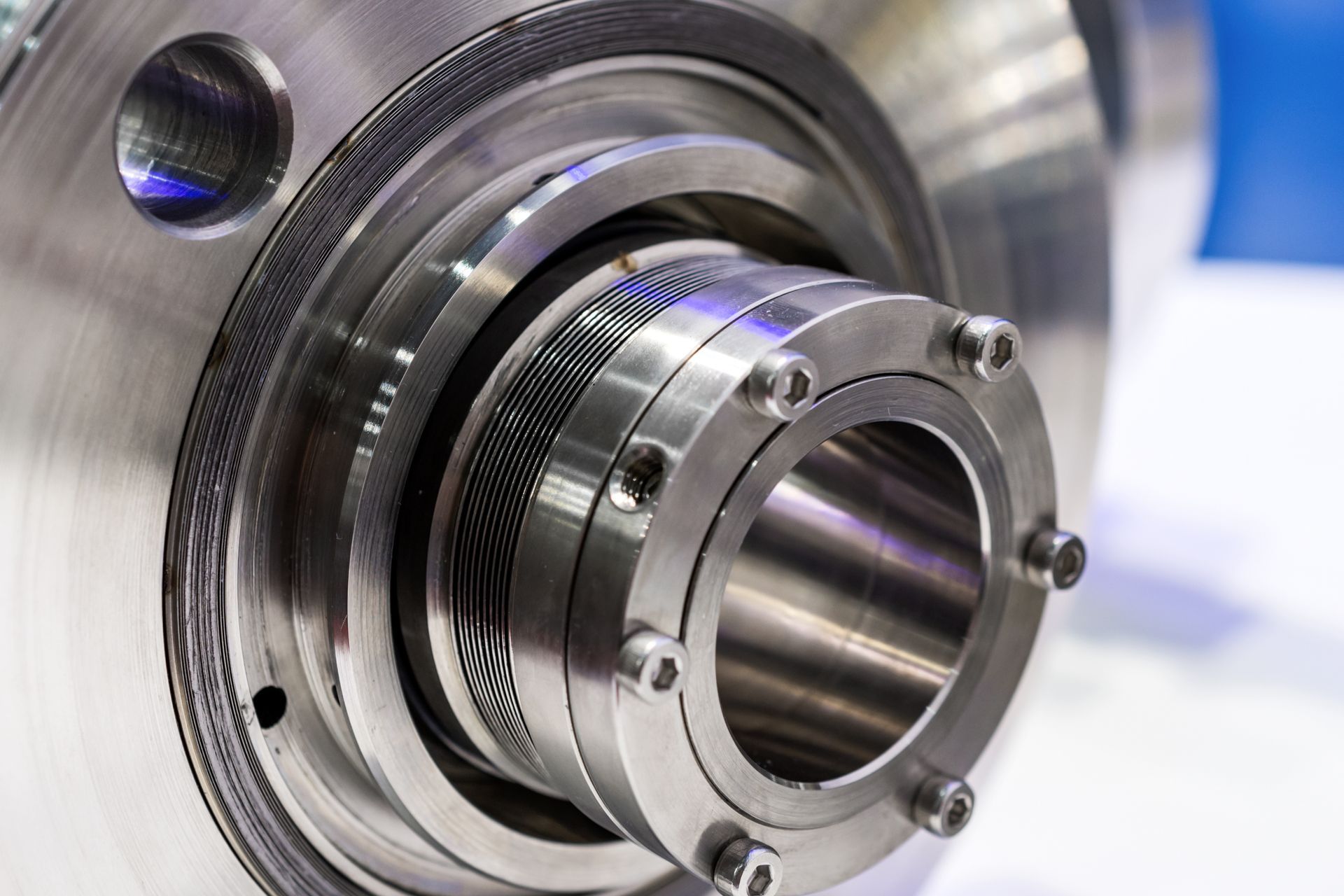 Close-up of a polished metal mechanical component with circular grooves and bolts.