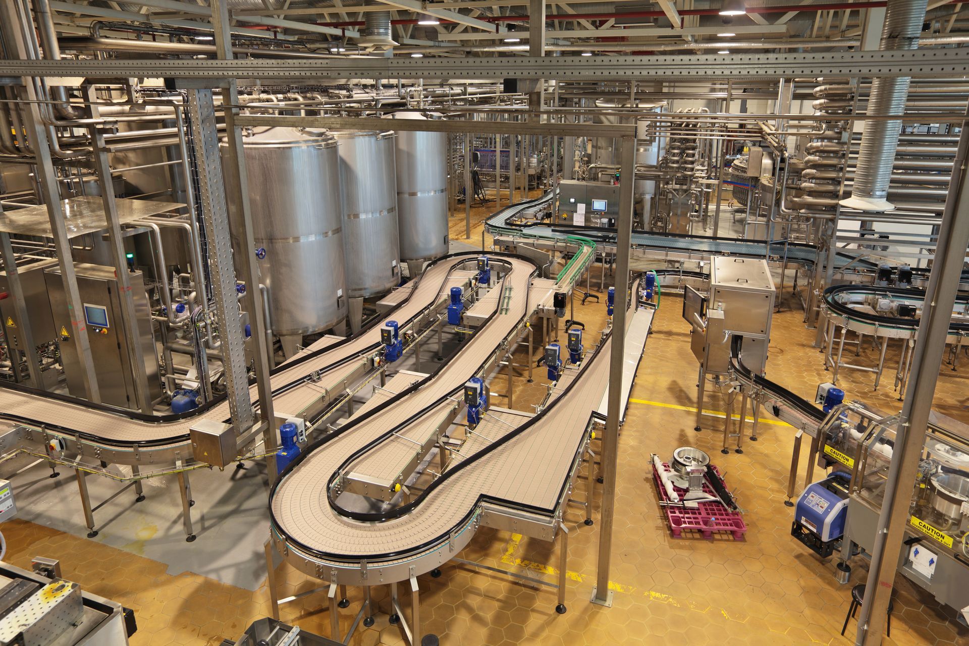Factory floor with conveyor belts, large metal tanks, and workers in blue uniforms.