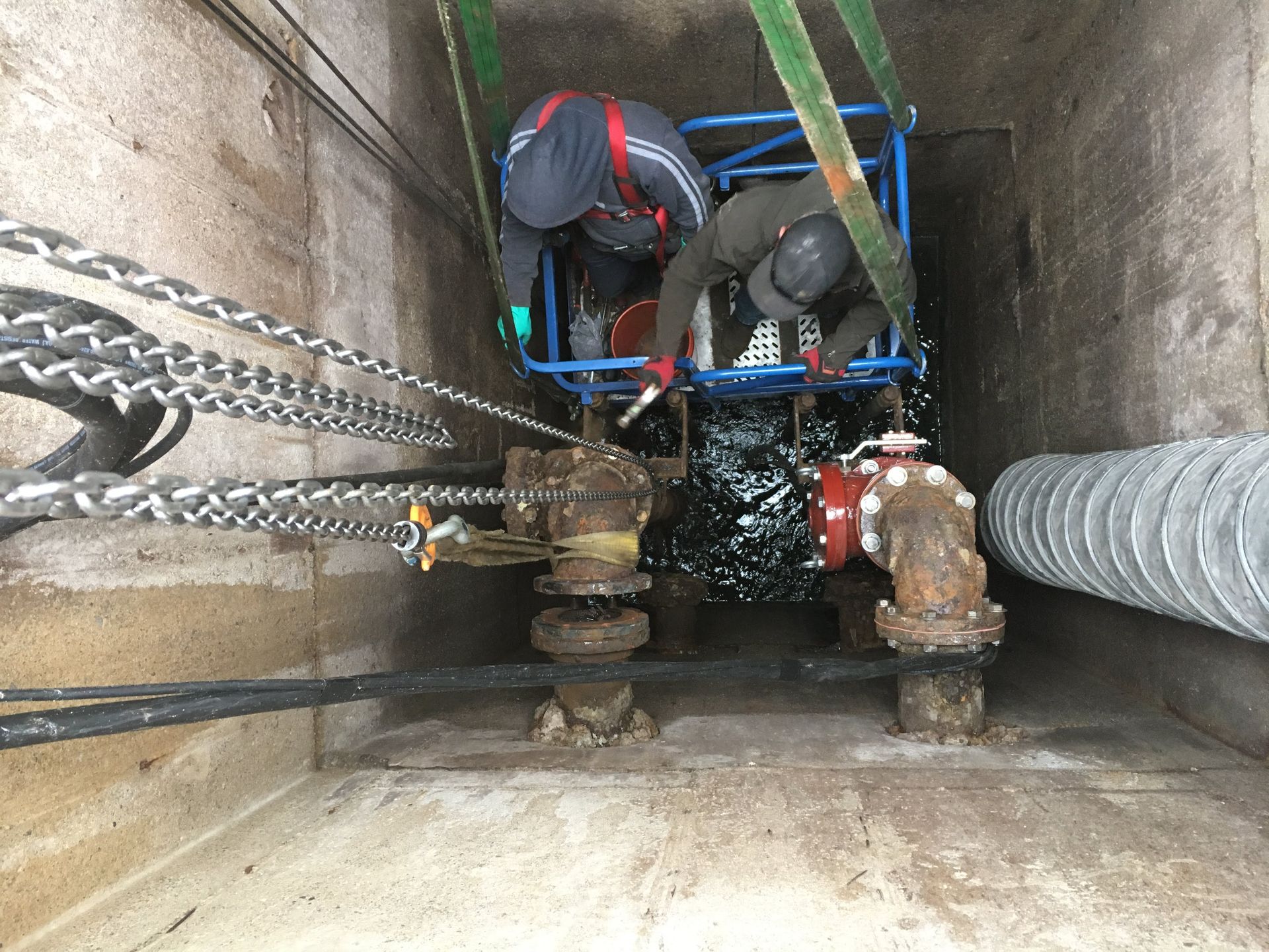 Two men are working on a pipe in a tunnel.